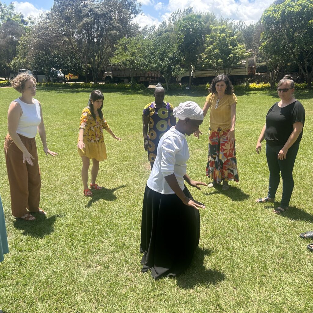 People stand in a circle on grass with a woman dancing in the center