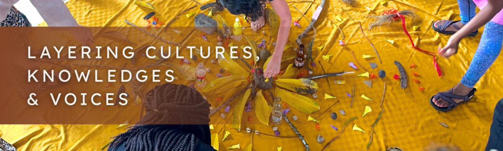 photo shows yellow fabric with objects on top in a mandala and people's heads and hands placing objects on it