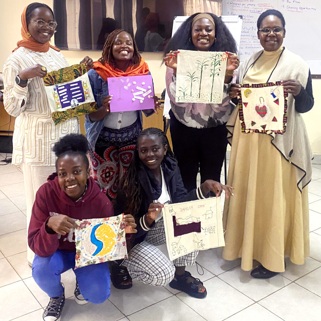 Four people stand holding up a work of art and two other people kneel in front of them, holding up art